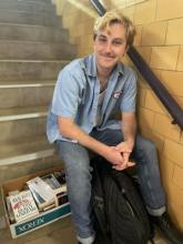 Parker sits on stairs of rodeo arena in Hustler shirt and books