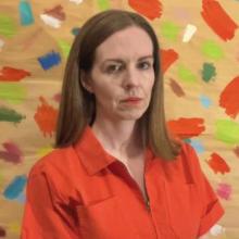 A picture of Laura Paul wearing an orange jumpsuit in front of a background of colorful brushstrokes.